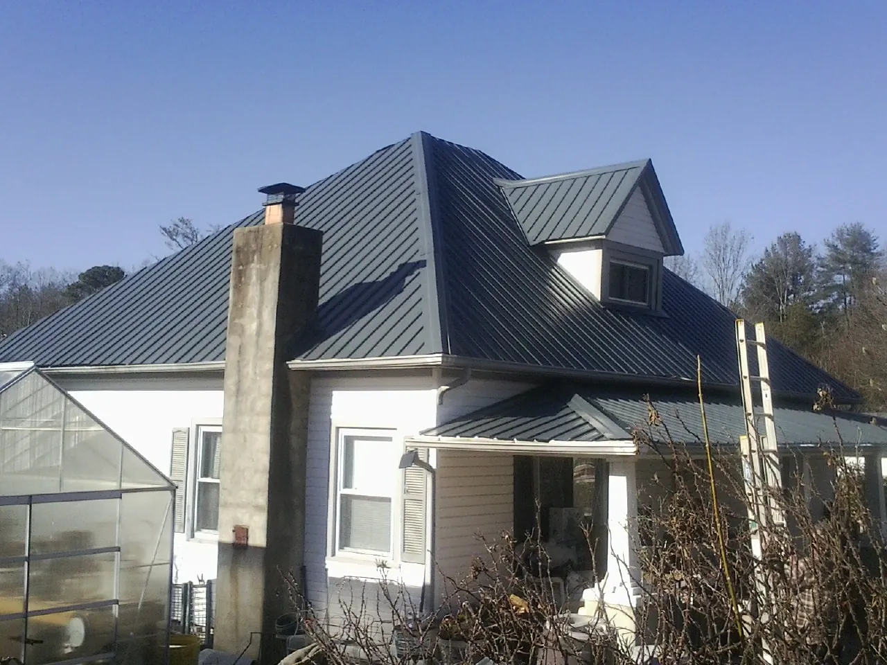 Dark blue standing seam metal roof on a white farmhouse with dormer — Slate & Tile Roof Repair by Roofing Brothers in Loon Lake
