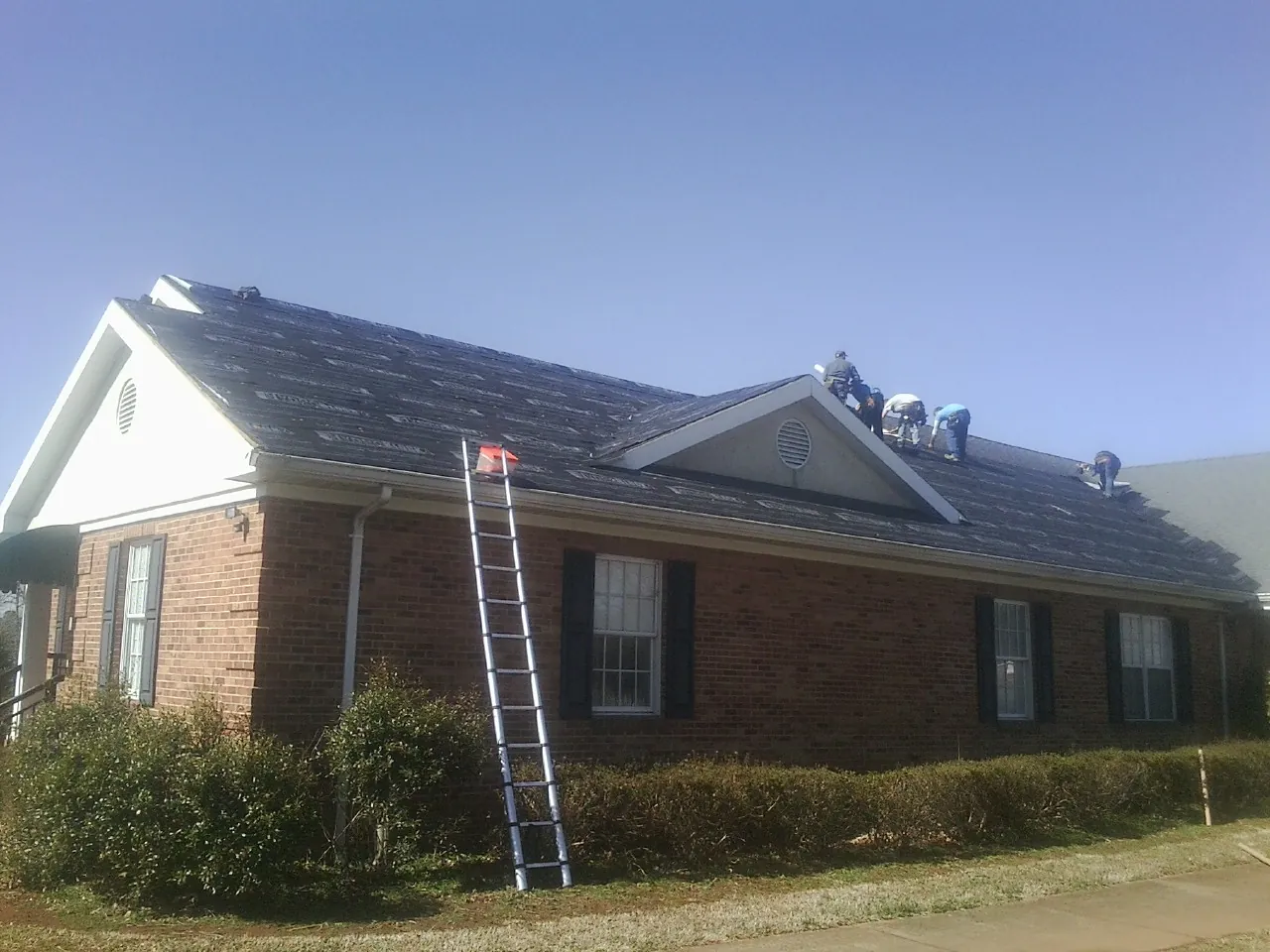 Crew tearing shingles off a brick ranch roof with a ladder set — Emergency Roof Repair work by our crew in Loon Lake