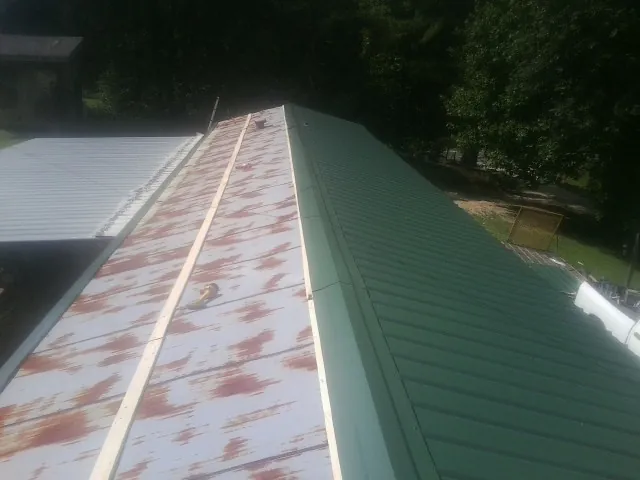 Old rusted panels beside newly installed green metal roofing — Wind Damage Roof Repair by Roofing Brothers in Loon Lake