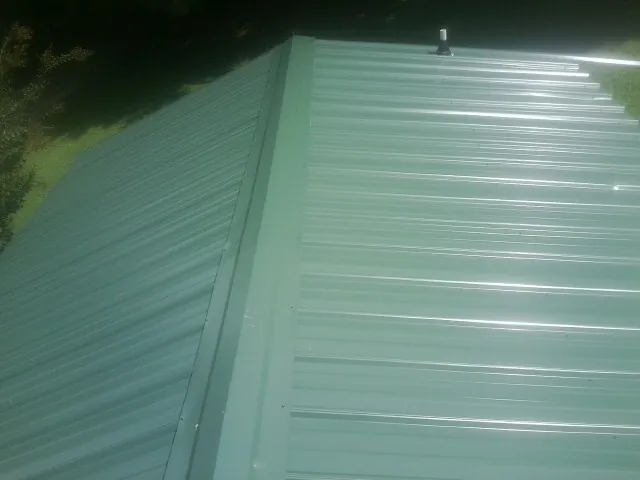 New green metal panels meeting at the ridge of a roof — Flat Roof Repair work by our crew in Loon Lake
