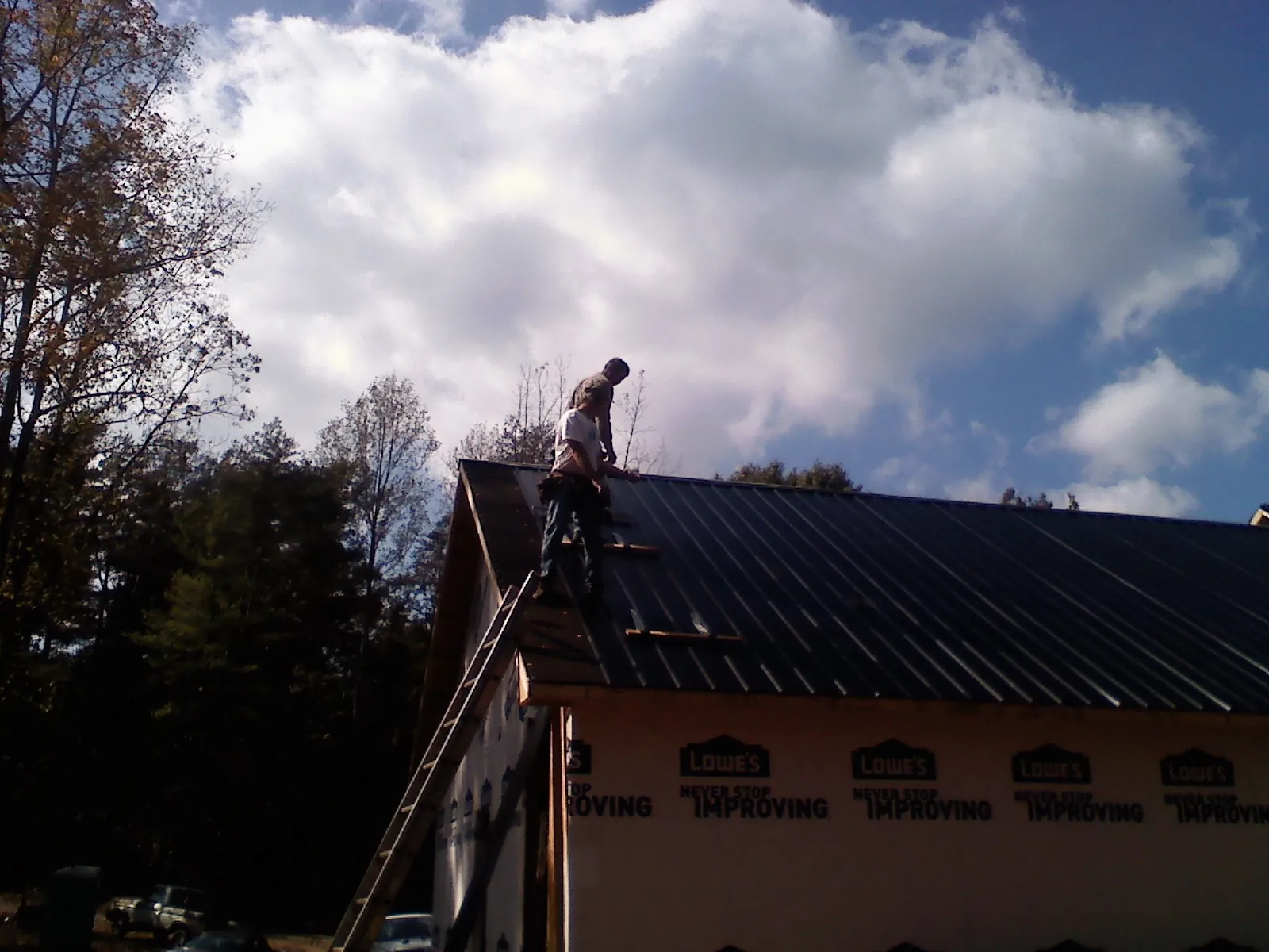 Roofer fastening dark metal panels high against a cloudy sky, from a Roof Inspection job in Loon Lake