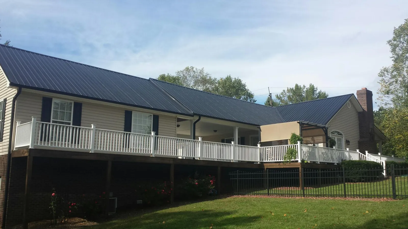 Black metal roof above a long white railed deck on a hillside home in Loon Lake