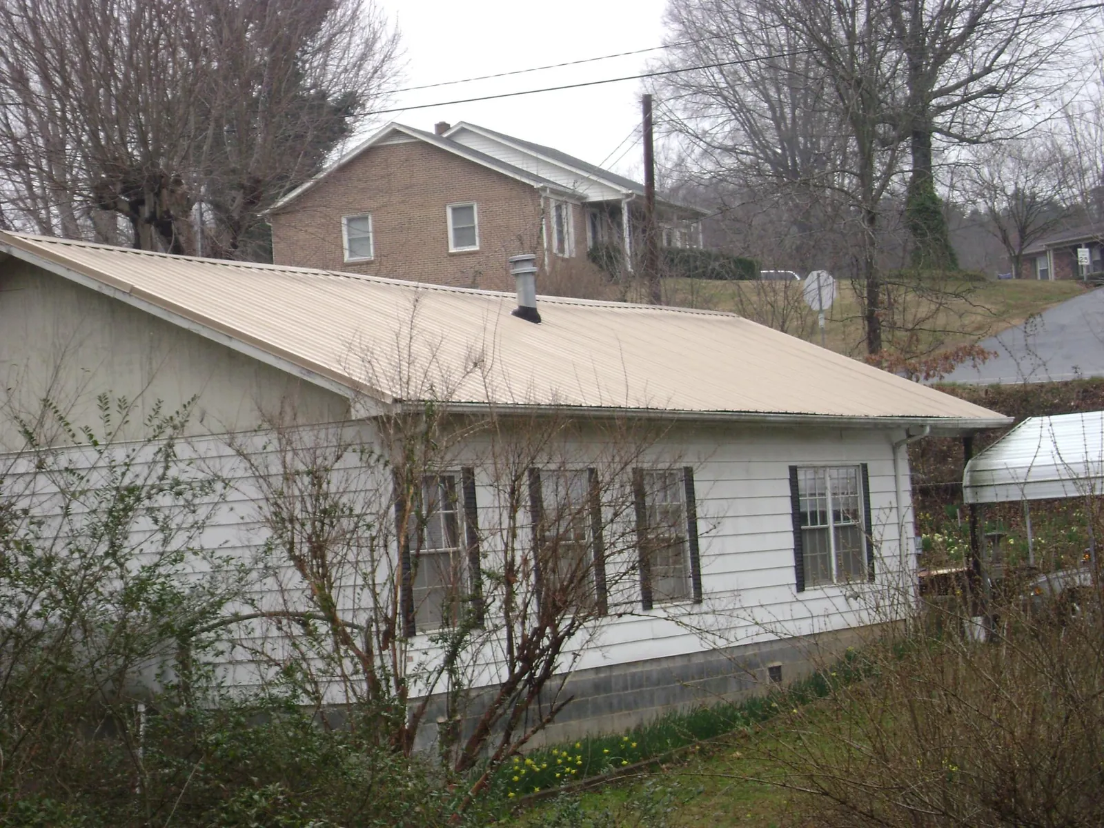 Tan metal roof on a white sided house set into a hillside — Commercial Roofing by Roofing Brothers in Loon Lake