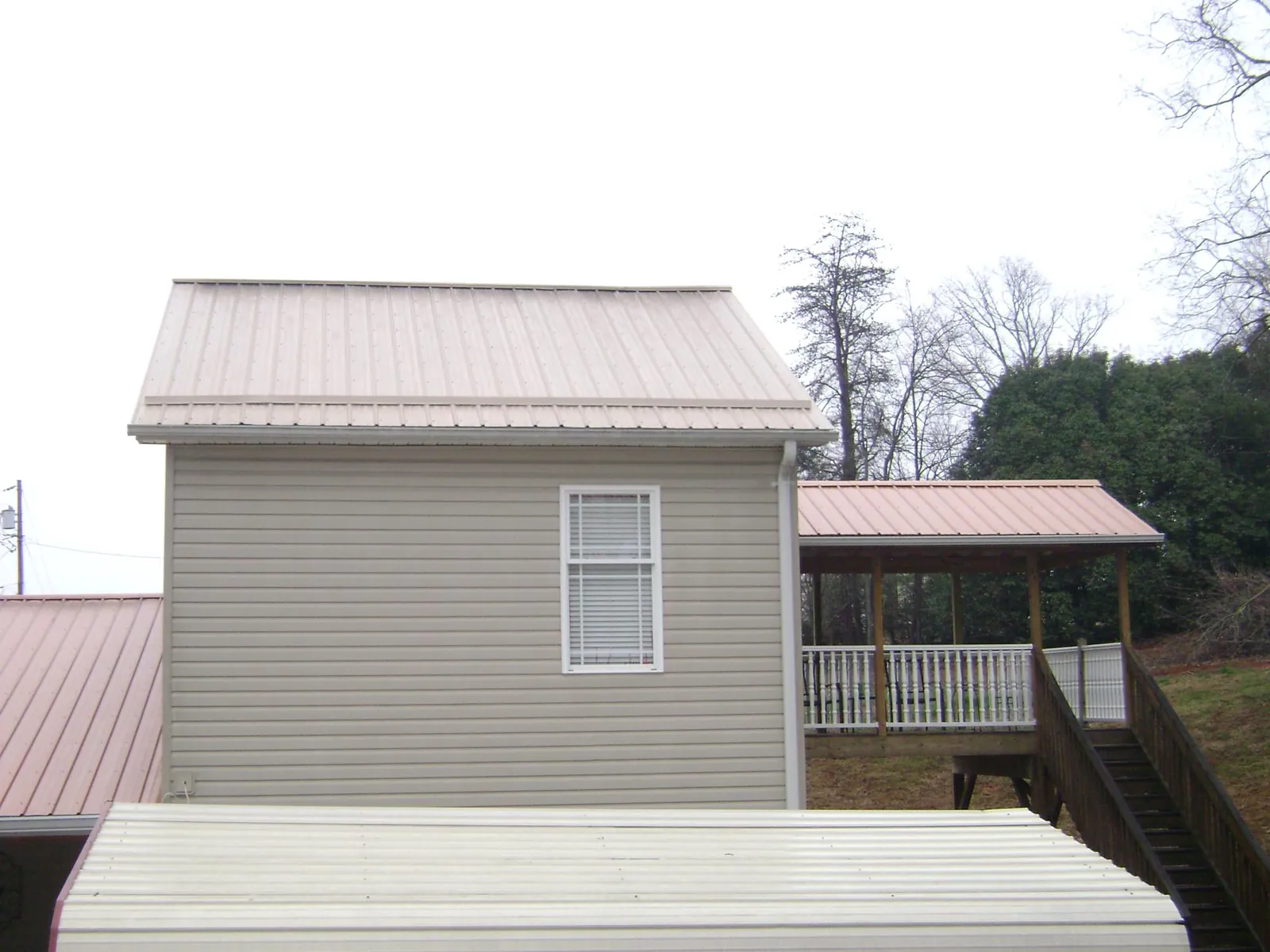 Tan metal roofs on a two story addition and attached porch, from a Roof Replacement job in Loon Lake